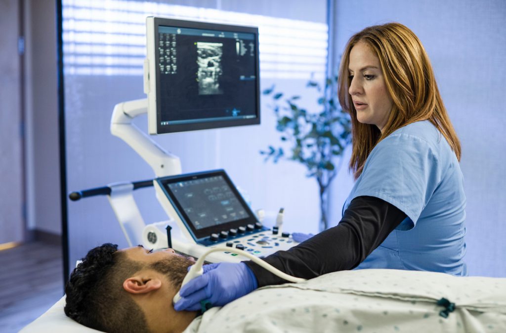 A Registered Vascular Specialist (RVS) performing a vascular ultrasound on a man's neck